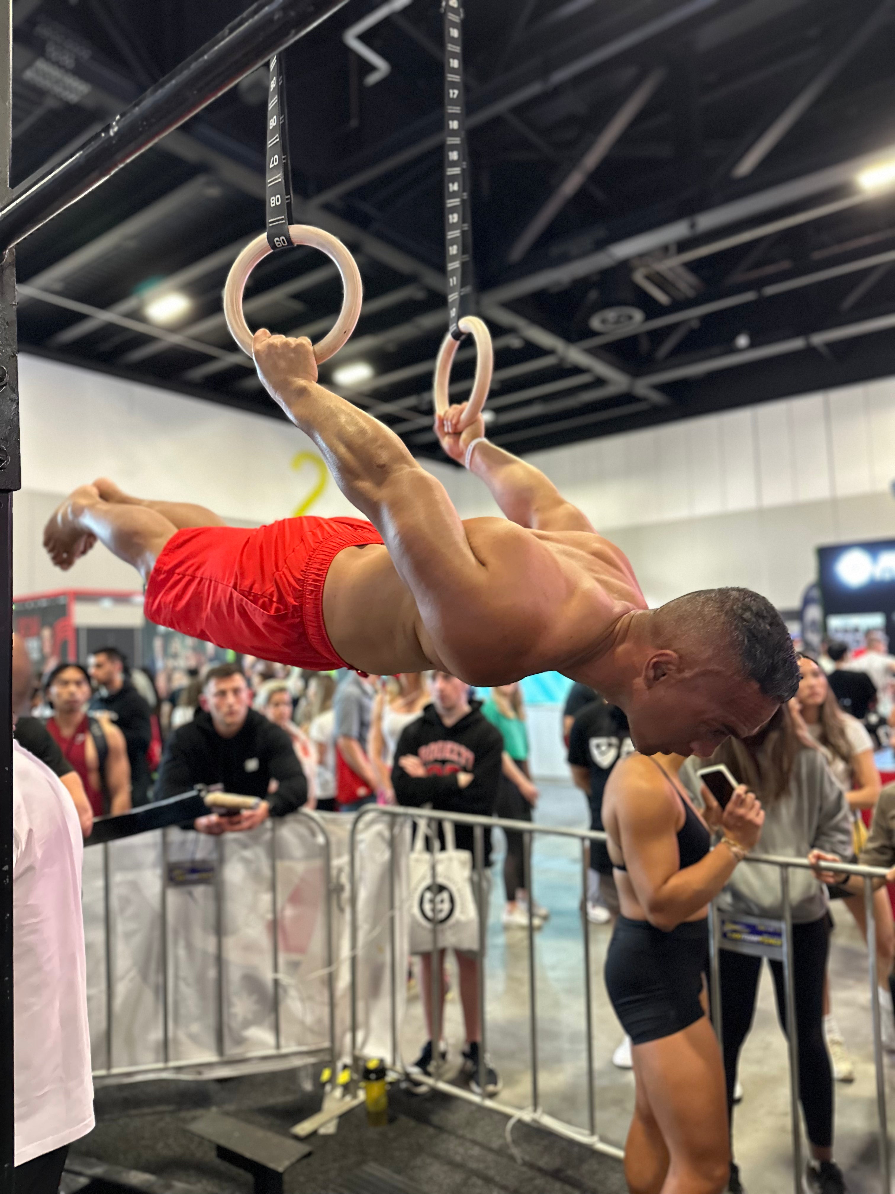 Person performing on rings at a gym with spectators watching.